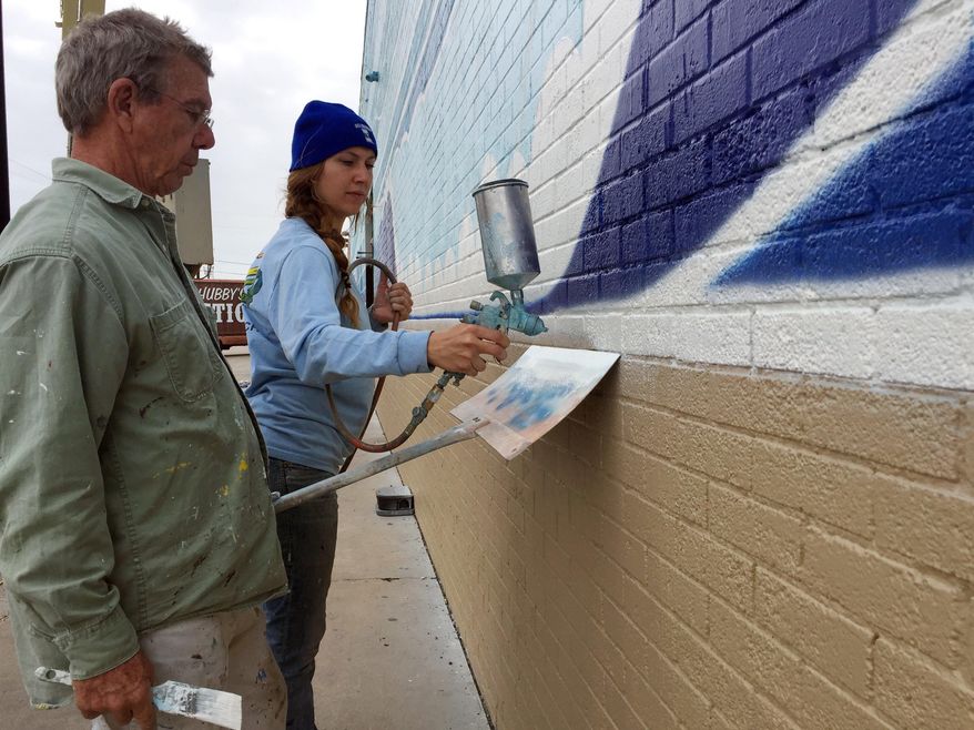In this Wednesday, Dec. 5, 2018 photo, artists John Olvey and Kaleigh Glover paint a mural on the side of the Corpus Christi Trade Center on in Corpus Christi, Texas. The pair spent eight days working on the 200-foot (61-meter) outdoor artwork, which features beach scenery with crashing waves and palm trees.(Mark Young/Corpus Christi Caller-Times via AP)