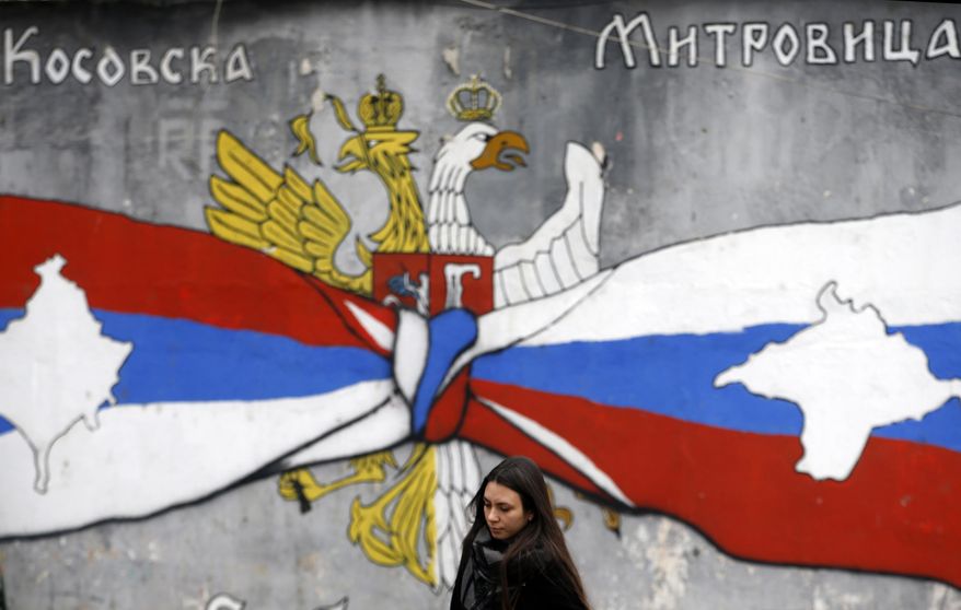 A woman walks by graffiti showing the Serbian flag, left, and Russian flags with maps of Kosovo and Crimea in northern, Serb-dominated part of ethnically divided town of Mitrovica, Kosovo, Saturday, Dec. 15, 2018. Serbia threatened a possible armed intervention in Kosovo after the Kosovo parliament on Friday overwhelmingly approved the formation of an army. Russia denounced the move to form a Kosovo army, saying the ethnic Albanian force must be &amp;quot;disbanded&amp;quot; by NATO in Kosovo. (AP Photo/Darko Vojinovic)