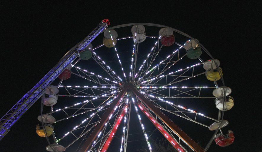 In this Saturday, Dec. 15, 2018 photo, firefighters work to disembark passengers from a Ferris wheel that malfunctioned in downtown Conway, Ark. A pivot pin holding one of the Ferris wheel's cylinders in place broke. All passengers were safely rescued. (Jeanette Anderton/Log Cabin Democrat via AP)