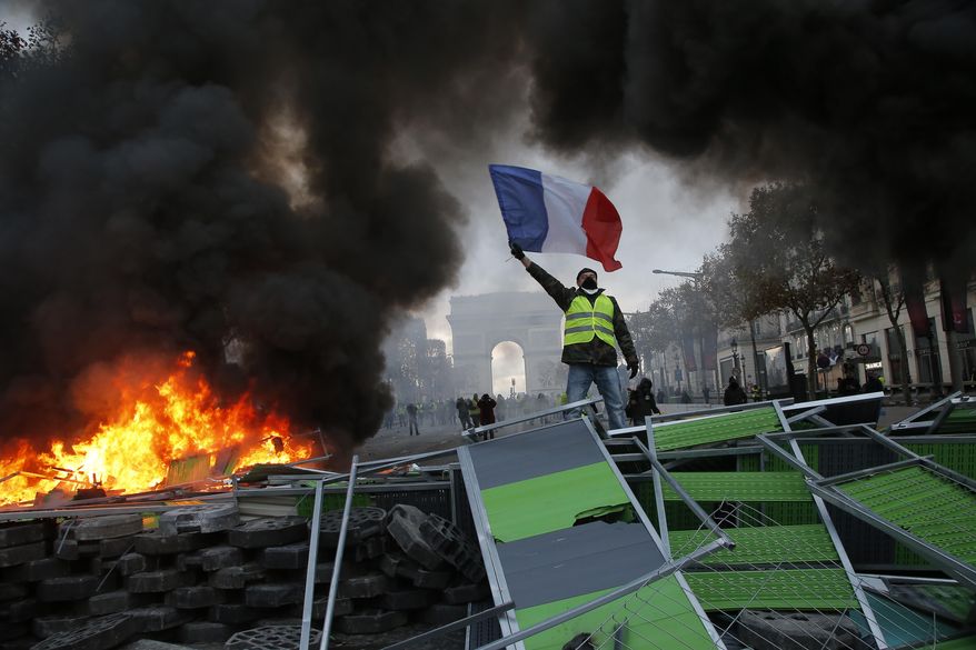 FILE - In this Saturday, Nov. 24, 2018 file photo a demonstrator waves the French flag onto a burning barricade on the Champs-Elysees avenue during a demonstration against the rising of the fuel taxes in Paris. (AP Photo/Michel Euler, File)