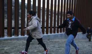 Honduran migrants run away from Border Patrol agents as they try to cross over the U.S. border wall to San Diego, California, from Tijuana, Mexico, Saturday, Dec. 15, 2018. (AP Photo/Moises Castillo)