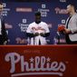 Philadelphia Phillies new outfielder Andrew McCutchen, center, accompanied by general manager Matt Klentak, left, and manager Gabe Kapler, puts on his uniform during a news conference in Philadelphia, Tuesday, Dec. 18, 2018. McCutchen and the Philadelphia Phillies finalized a back-loaded $50 million, three-year contract last week, a deal that includes a team option for 2022. (AP Photo/Matt Rourke)