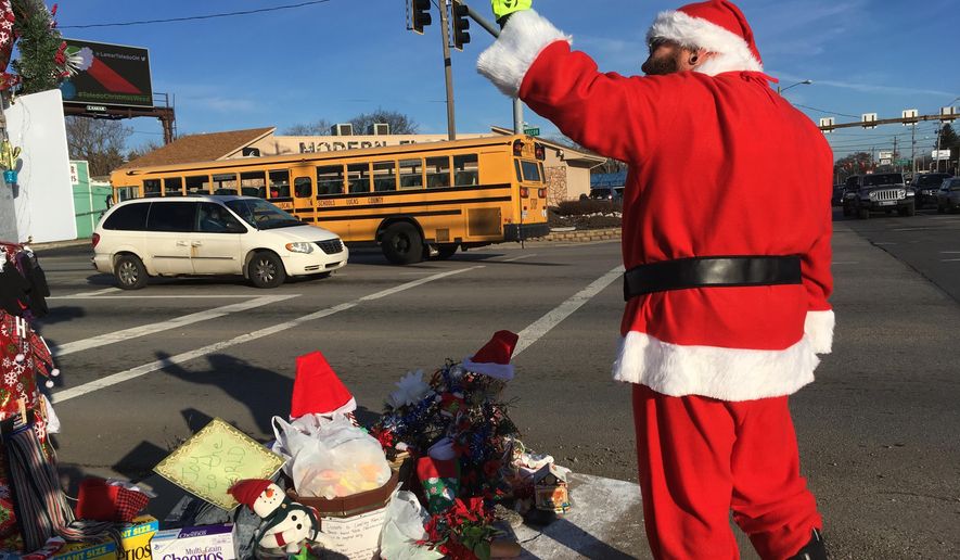 In this Dec. 18, 2018 photo, Jimmy Izbinski, wearing a Santa suit, waves to motorists passing the Christmas weed in Toledo, Ohio. The street corner weed decked out with lights and ornaments is spreading holiday goodwill. (AP Photo/John Seewer)