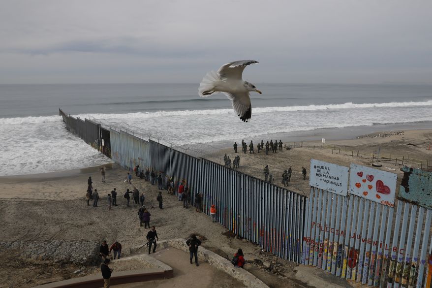 In this Dec. 10, 2018, file photo, people look on from the Mexican side, left, as U.S. Border Patrol agents on the other side of the U.S. border wall in San Diego prepare for the arrival of hundreds of pro-migration protestors, seen from Tijuana, Mexico. A relentless stream of U.S. policy shifts in 2018 has amounted to one of the boldest attacks on all types of immigration that the country has ever seen. Some see it as a tug-of-war between foundational national ideals and a fight for a new path forward led by President Donald Trump. (AP Photo/Rebecca Blackwell) **FILE**