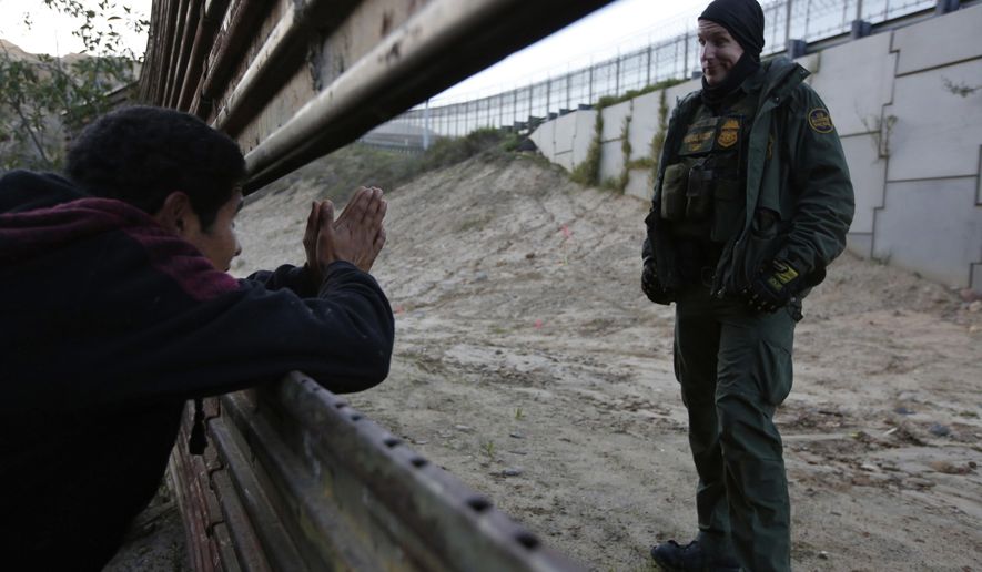 A Honduran migrant pleads with a U.S. Border Patrol agent to let him cross into the U.S., as he peeks through a barrier in Tijuana, Mexico, on Saturday, Dec. 15, 2018. The officer did not respond, and the Honduran did not know the agent would not prevent him from crossing. The man returned to the group of people he was with. (AP Photo/Moises Castillo)