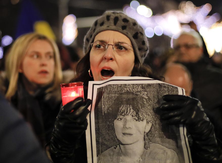 A woman held a photograph of a 1989 uprising victim while singing the national anthem along with others during a protest in Bucharest on Saturday. More than 1,000 Romanians have demanded more democracy. (Associated Press)