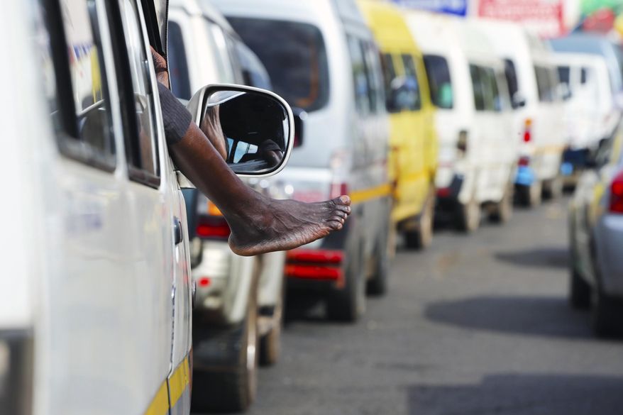 In this photo taken on Friday Dec, 21, 2018, a driver takes a nap with his feet sticking out of the car while in a fuel queue in Harare. The Christmas lights are up in Zimbabwe's capital but the mood is less than festive as the country grapples with an economic crisis that prevents many families from enjoying the holiday season. Zimbabwe is experiencing its worst economic meltdown in a decade. (AP Photo/Tsvangirayi Mukwazhi)