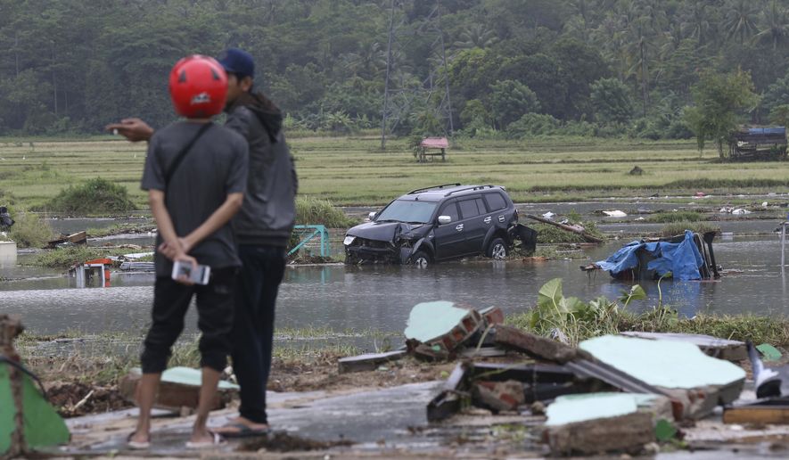 Villagers stand near a car damaged by a tsunami in Carita, Indonesia, Sunday, Dec. 23, 2018. The tsunami occurred after the eruption of a volcano around Indonesia&#39;s Sunda Strait during a busy holiday weekend, sending water crashing ashore and sweeping away hotels, hundreds of houses and people attending a beach concert. (AP Photo/Achmad Ibrahim)
