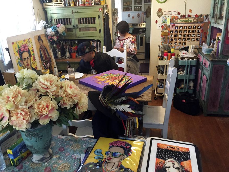 In this Thursday, April 5, 2018 photo artist Moises Salcedo (left) of Albuquerque, who goes by the name El Moises, sits amid his artwork at his home and studio in Albuquerque, N.M. on Thursday, April 5, 2018. He and celebrated Chicano author Rudolfo Anaya crafted the book that follows the adventures in English and Spanish of a tiny owl named Oli who longs to read on his own, even as he skips school and tangles with a cast of conniving animal characters in the hills and skies of northern New Mexico. A sequel is planned to address concerns about bullying. (AP Photo/Morgan Lee)