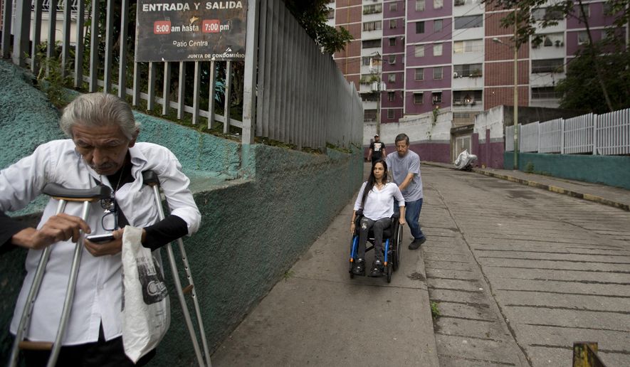 In this Dec. 17, 2018 photo, neighbor Dixon Rosales helps dancer Iraly Yanez negotiate her wheelchair on a downhill path, in Caracas, Venezuela. A stray bullet crushed Yanez's aspirations of becoming a professional dancer eight years ago as it ruptured two of her vertebrae and left her paraplegic. (AP Photo/Fernando Llano)
