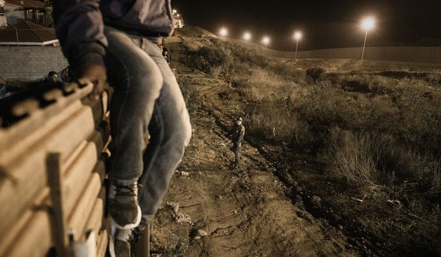 A migrant jumps into the United States to San Diego, from Tijuana, Mexico, in front of a border patrol officer on Tuesday, Dec. 25, 2018. Discouraged by the long wait to apply for asylum through official ports of entry, many Central American migrants from recent caravans are choosing to cross the U.S. border wall and hand themselves into border patrol agents. (AP Photo/Daniel Ochoa de Olza)