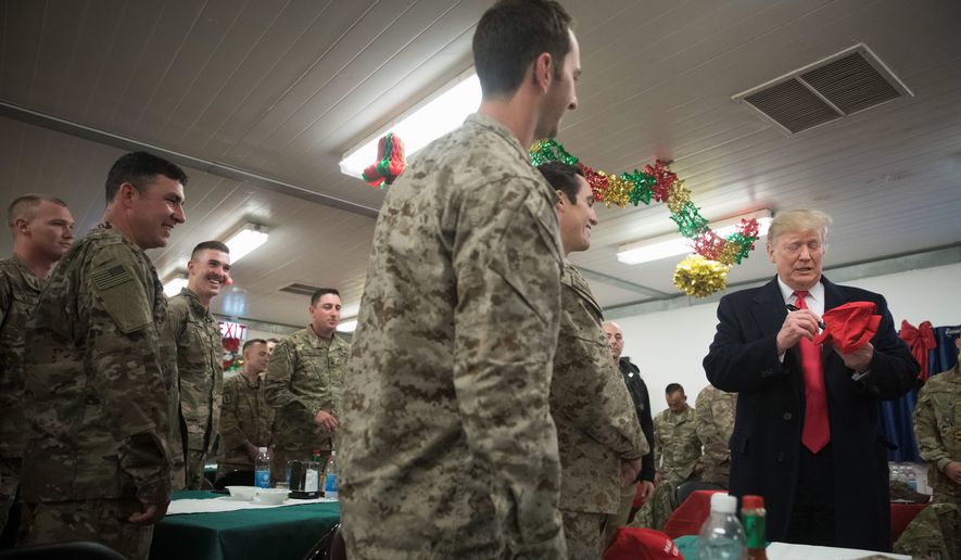 President Trump signs a Make America Great Again hat as he visits with members of the military at a dining hall at Al Asad Air Base, Iraq, on Wednesday. A former Pentagon spokesman blasted both Mr. Trump and the soldier for event. (Associated Press)