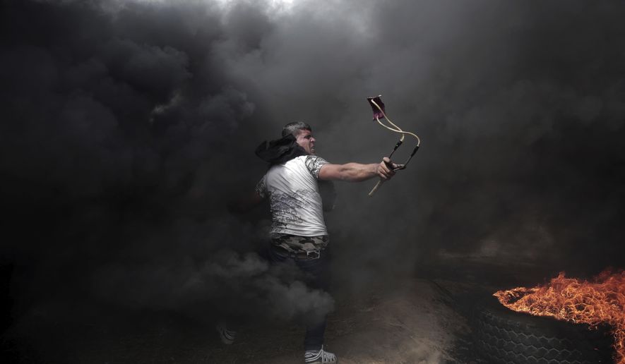 A Palestinian protester hurls stones at Israeli troops during a protest at the Gaza Strip&#x27;s border with Israel, Friday, April 20, 2018, during a weekly protest on Gaza&#x27;s border with Israel. (AP Photo/ Khalil Hamra)