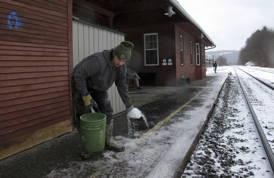 Matteo Perantoni spreads ice melt on the platform on Friday, Dec. 28, 2018, at the Montpelier-Berlin Amtrak train station in Berlin, Vt. A winter storm brought snow, sleet, freezing rain and rain to northern New England, making for a dangerous and slippery commute. (AP Photo/Lisa Rathke)
