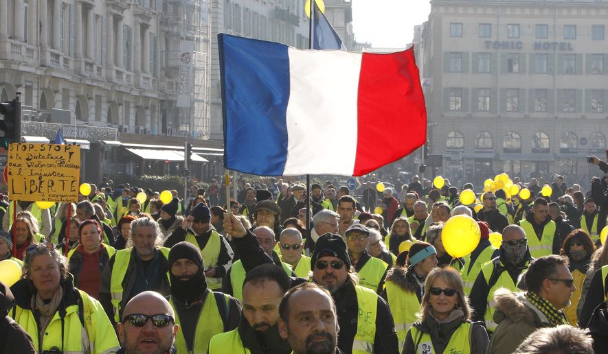 Demonstrators wearing their yellow vests brandish a French flag during a demonstration in Marseille, southern France, Saturday, Dec. 29, 2018.  The yellow vest movement held several peaceful demonstrations in cities and towns around France, including about 1,500 people who marched through Marseille. (AP Photo/Claude Paris)