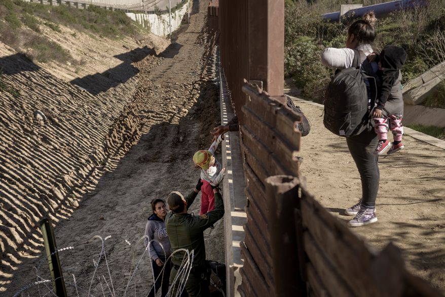 A Border Patrol officer holds a baby as he helps a migrant to go down after they jump the border fence to get into the U.S. side to San Diego, Calif., from Tijuana, Mexico, Saturday, Dec. 29, 2018. Discouraged by the long wait to apply for asylum through official ports of entry, many migrants from recent caravans are choosing to cross the U.S. border wall and hand themselves in to border patrol agents. (AP Photo/Daniel Ochoa de Olza)