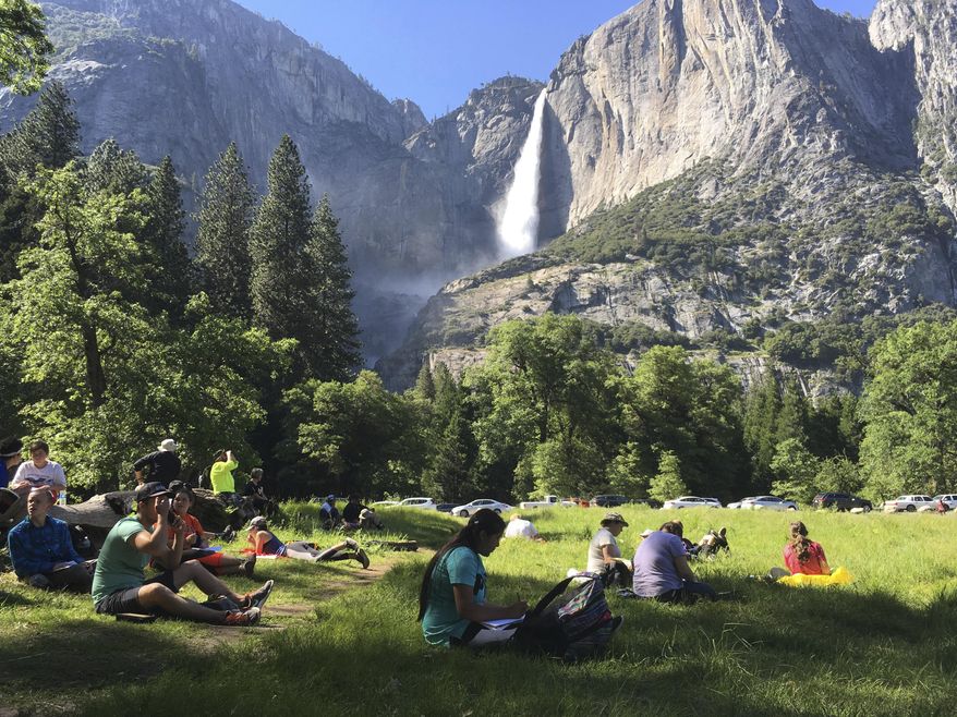FILE - In this May 25, 2017 file photo, a class of eighth-grade students and their chaperones sit in a meadow at Yosemite National Park, Calif., below Yosemite Falls. Some of the West’s iconic national parks are beginning to partially close as they deal with overflowing restrooms and vandals on the 10th day of a federal government shutdown. (AP Photo/Scott Smith, File)