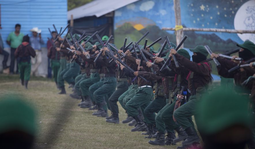 Members of the Zapatista National Liberation Army, EZLN, march into the plaza brandishing sticks during an event marking the 25th anniversary of the Zapatista uprising, in La Realidad, Chiapas state, Mexico, Monday, Dec. 31, 2018. (AP Photo/Eduardo Verdugo)
