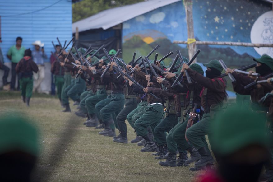 Members of the Zapatista National Liberation Army, EZLN, march into the plaza brandishing sticks during an event marking the 25th anniversary of the Zapatista uprising, in La Realidad, Chiapas state, Mexico, Monday, Dec. 31, 2018. (AP Photo/Eduardo Verdugo)