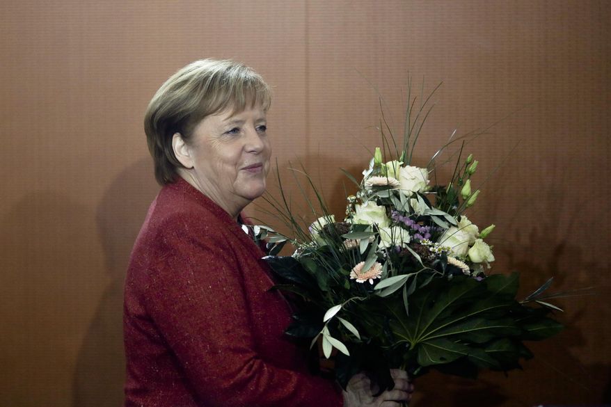 German Chancellor Angela Merkel arrives with flowers for the weekly cabinet meeting of the German government at the chancellery in Berlin, Germany, Wednesday, Jan. 9, 2019. The flowers are a birthday present for the Government's Commissioner for Culture and the Media, Monika Gruetters. (AP Photo/Markus Schreiber)