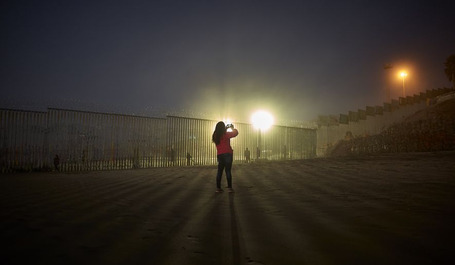 A woman records with her phone, as floodlights from the United States light up the border wall, topped with razor wire, Thursday, Jan. 10, 2019, along the beach in Tijuana, Mexico. Taking the shutdown fight to the Mexican border, U.S. President Donald Trump edged closer Thursday to declaring a national emergency in an extraordinary end run around Congress to fund his long-promised border wall. (AP Photo/Gregory Bull)