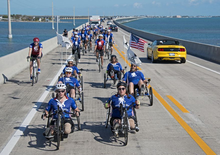 In this photo provided by the Florida Keys News Bureau, injured military personnel including Army Staff Sgt. Sam Oelke, left, retired Air Force Staff Sgt. Jennifer Caudillo, right, and other wounded military personnel ride bicycles on the Seven Mile Bridge during the Florida Keys Soldier Ride Friday, Jan. 11, 2019, near Marathon, Fla. Some 45 men and women are riding bicycles down segments of the Florida Keys Overseas Highway as a facet of an effort organized by the Wounded Warrior Project to raise public awareness and support for the needs of severely injured members of the U.S. military. (Andy Newman/Florida Keys News Bureau via AP)