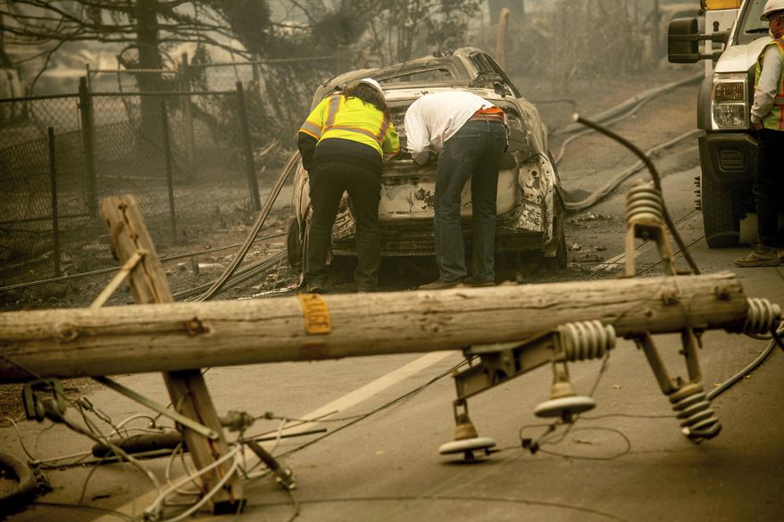 FILE - In this Nov. 10, 2018 file photo, with a downed power utility pole in the foreground, Eric England, right, searches through a friend&#x27;s vehicle after the wildfire burned through Paradise, Calif. Facing potentially colossal liabilities over deadly California wildfires, PG&amp;amp;E will file for bankruptcy protection. The announcement Monday, Jan. 14, 2019, follows the resignation of the power company’s chief executive. (AP Photo/Noah Berger, File)