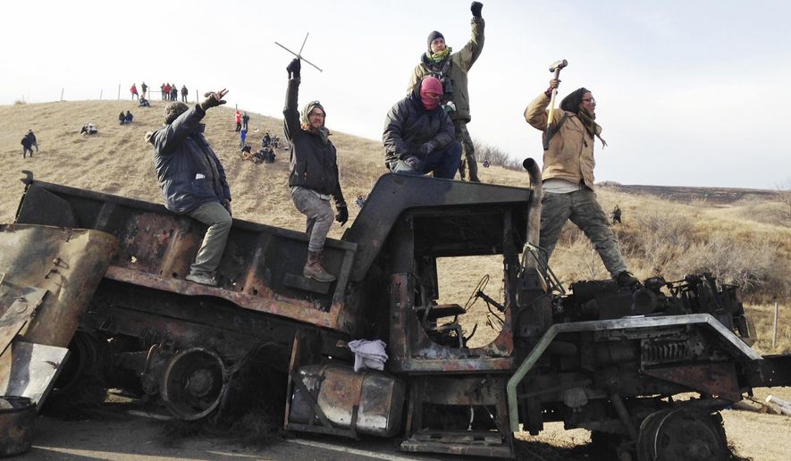 FILE - In this Nov. 21, 2016 file photo, protesters against the Dakota Access oil pipeline stand on a burned-out truck near Cannon Ball, N.D. North Dakota officials including Gov. Doug Burgum want a federal judge to dismiss a civil rights lawsuit filed over a five-month shutdown of a portion of state Highway 1806 during protests against the Dakota Access oil pipeline. Attorneys for the state and Morton County say the shutdown for public safety was warranted because of the "mayhem" caused by pipeline protesters in 2016 and early 2017. (AP Photo/James MacPherson, File)