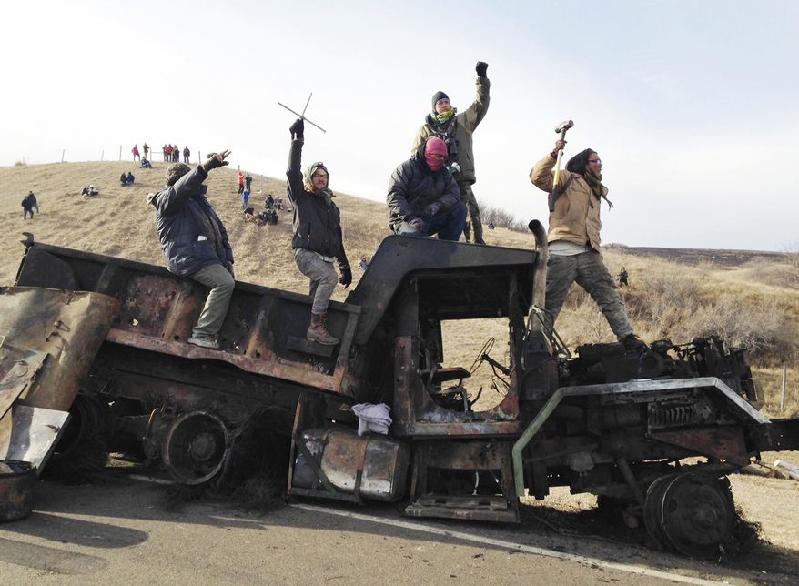 FILE - In this Nov. 21, 2016 file photo, protesters against the Dakota Access oil pipeline stand on a burned-out truck near Cannon Ball, N.D. North Dakota officials including Gov. Doug Burgum want a federal judge to dismiss a civil rights lawsuit filed over a five-month shutdown of a portion of state Highway 1806 during protests against the Dakota Access oil pipeline. Attorneys for the state and Morton County say the shutdown for public safety was warranted because of the "mayhem" caused by pipeline protesters in 2016 and early 2017. (AP Photo/James MacPherson, File)