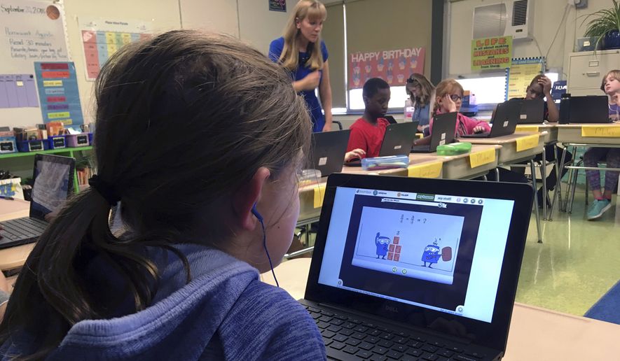 In this Sept. 20, 2018 photo, fifth-grade student Ashlynn De Filippis, left, works math problems on the DreamBox system as teacher Heather Dalton, center rear, works with other students in class at Charles Barnum Elementary School in Groton, Conn. A wide array of apps, websites and software used in schools borrow elements from video games to help teachers connect with students living technology-infused lives. (AP Photo/Michael Melia)