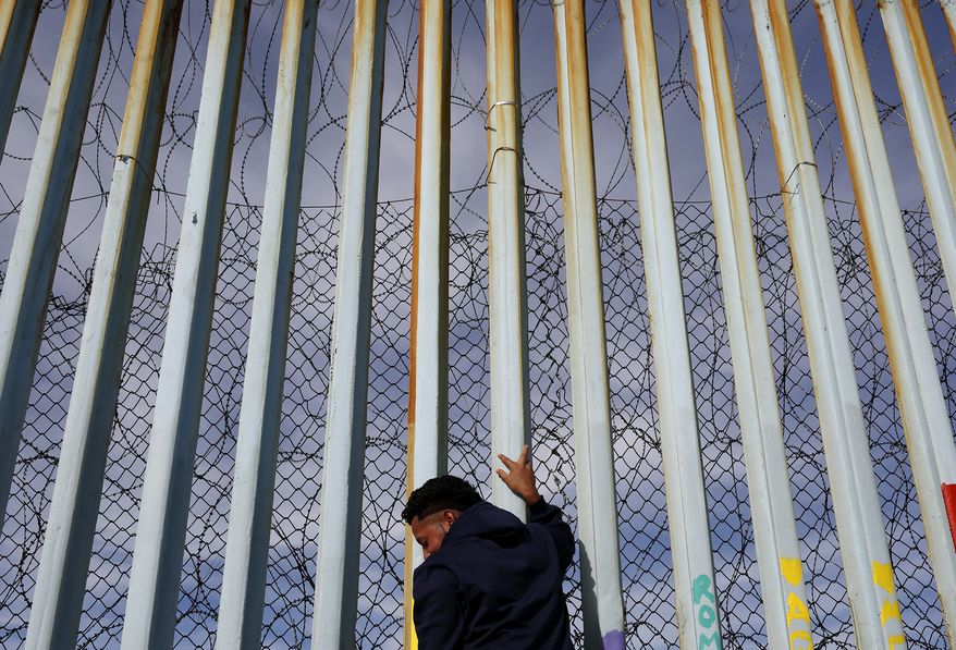 FILE - In this Jan. 8, 2019, file photo, a man holds on to the border wall along the beach, in Tijuana, Mexico. The migrant caravan that was seized upon by U.S. President Donald Trump in the run-up to the 2018 election has quietly dwindled to a few hundred people, with many of them having crossed into the U.S. or put down roots in Mexico. (AP Photo/Gregory Bull, File)