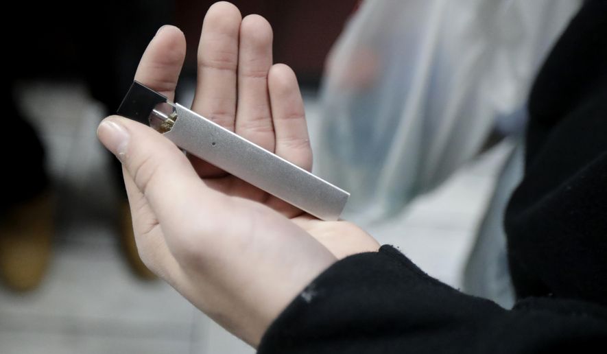 FILE - In this  Dec. 20, 2018, file photo, a man displays his Juul electronic cigarette while shopping at a convenience store in Hoboken, N.J. U.S. health officials are scrambling to keep e-cigarettes away from teenagers amid an epidemic of underage use. But doctors face a new dilemma: there are few effective options for weening young people off nicotine vaping devices like Juul. (AP Photo/Julio Cortez, File)