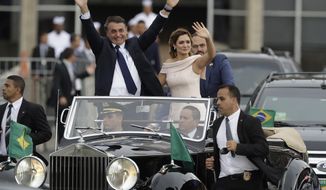 FILE - In this Jan. 1, 2019, file photo, flanked by first lady Michelle Bolsonaro, Brazil&#39;s President Jair Bolsonaro waves as he rides in an open car after his swearing-in ceremony in Brasilia, Brazil. The far-right leader’s first two weeks on the job have been filled with missteps and communication gaffes and little of his promised sweeping changes, underscoring a steep learning curve for a president elected on promises to overhaul much of daily life in Latin America&#39;s largest nation. (AP Photo/Andre Penner, File)