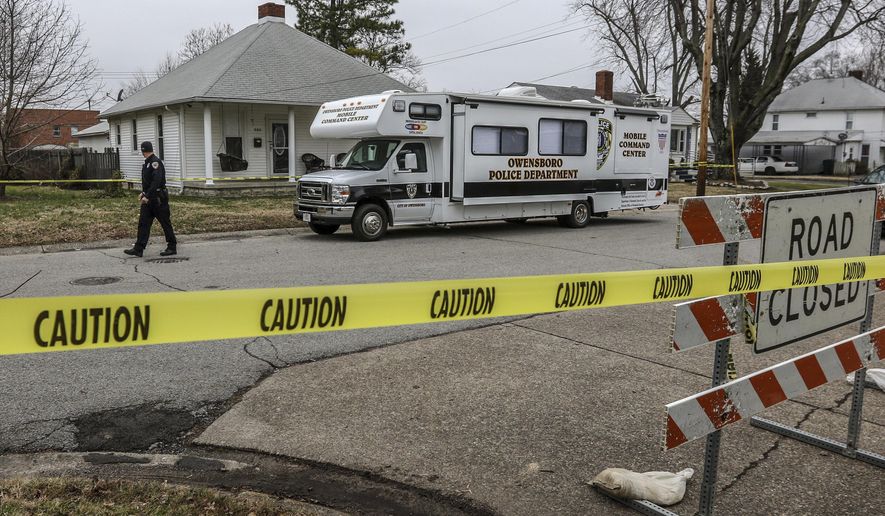 Officer Aron Contratto with the Owensboro Police Department, left, walks along the taped-off perimeter of the home at 940 Audubon Ave. where three people were found fatally shot Thursday morning in Owensboro. The Owensboro Police Department has charged two men in connection with the shootings. (Greg Eans/The Messenger-Inquirer via AP)