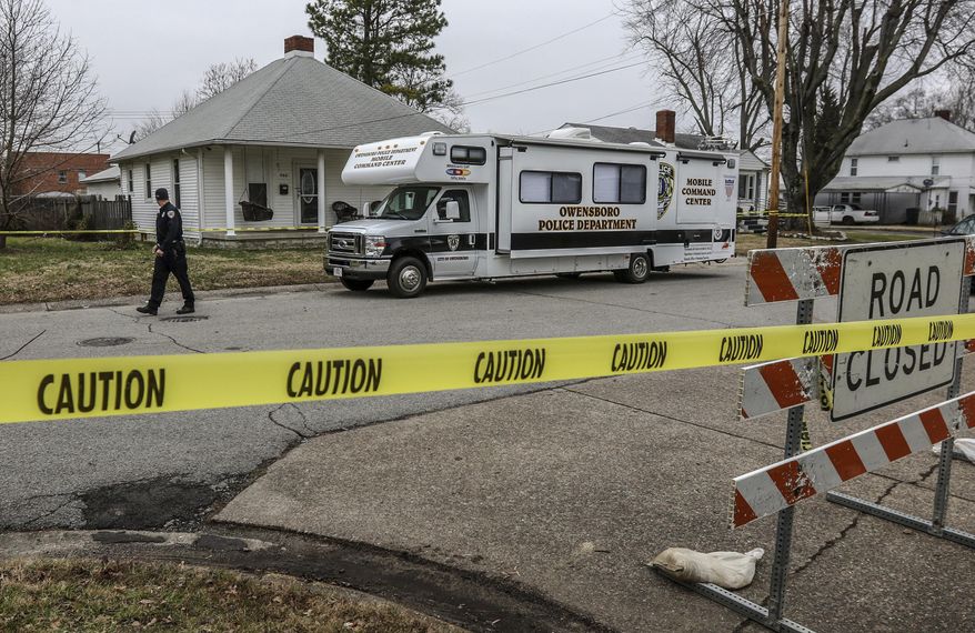 Officer Aron Contratto with the Owensboro Police Department, left, walks along the taped-off perimeter of the home at 940 Audubon Ave. where three people were found fatally shot Thursday morning in Owensboro. The Owensboro Police Department has charged two men in connection with the shootings. (Greg Eans/The Messenger-Inquirer via AP)
