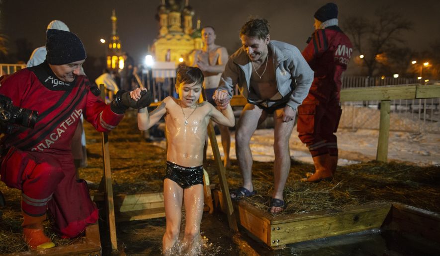 Russian Emergency Situations employees help a boy to bath in the icy water on Epiphany at the Church of the Holy Trinity in Ostankino near TV Tower in Moscow, Russia, Friday, Jan. 18, 2019. Across Russia, the devout and the daring are observing the Orthodox Christian feast day of Epiphany by immersing themselves in frigid water through holes cut through the ice of lakes and rivers. Epiphany celebrates the revelation of Jesus Christ as the incarnation of God through his baptism in the River Jordan. (AP Photo/Alexander Zemlianichenko)