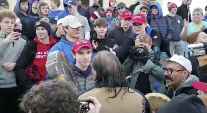 In this Friday, Jan. 18, 2019, image made from video provided by the Survival Media Agency, a teenager wearing a &quot;Make America Great Again&quot; hat, center left, stands in front of an elderly Native American singing and playing a drum in Washington. (Survival Media Agency via Associated Press) **FILE**