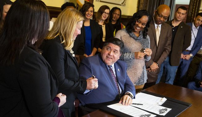 FILE - In this Jan. 15, 2019 file photo, Illinois Gov. J.B. Pritzker, center, is seen at the signing of a bill that prohibits employers from asking about salary history in interviews, during a press conference in Springfield, Ill. Just days into his term of office, Gov. J.B. Pritzker signaled last week an abrupt about-face in government relations with organized labor during the past four years. The Democrat took a series of pro-worker actions, highlighted by reinstatement of long-postponed, experience-based salary increases for state workers represented by the American Federation of State, County and Municipal Employees. (Rich Saal/The State Journal-Register via AP File)