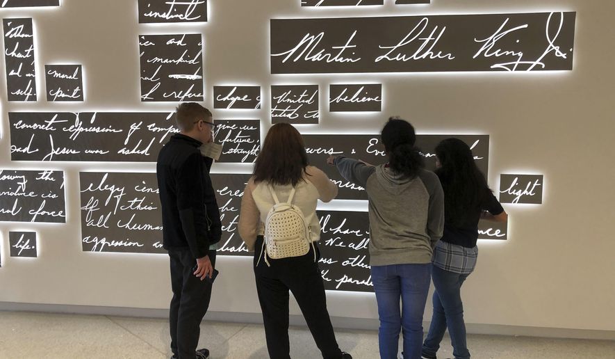 In this Friday, Jan. 18, 2019 photo, visitors look at a new metal sculpture at the National Center for Civil and Human Rights in Atlanta that features the words of the Rev. Martin Luther King Jr. in his own handwriting illuminated by light. The permanent sculpture hangs just outside a gallery where an exhibit of King's papers, including drafts of famous speeches and notable sermons, is on display. (AP Photo/Kate Brumback)