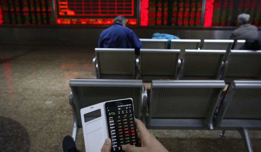 A man checks stock prices through his smartphone at a brokerage house in Beijing, Tuesday, Jan. 22, 2019. Asian markets were mostly lower on Tuesday after the International Monetary Fund trimmed its global outlook for 2019 and 2020. This came after China said its economy grew at the slowest pace in 30 years. (AP Photo/Andy Wong)