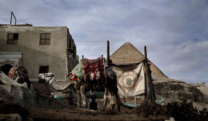 FILE - In this Dec. 6, 2017 file photo, a woman does early morning chores near the Great Pyramid, in Nazlet el-Samman, Giza, Egypt. Egyptian security officials said Monday, Jan. 21, 2019, that police arrested 24 people who tried to prevent authorities from removing illegal buildings near the Giza pyramids. They said police used tear gas to disperse residents and shopkeepers in the Nazlet el-Samman village after they scuffled with police escorting the demolition workers. (AP Photo/Nariman El-Mofty, File)