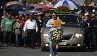 A woman carries a cross with the name Cesar Jimenez Brito during his funeral procession after he died when a gas pipeline exploded in the village of Tlahuelilpan, Mexico, Sunday Jan. 20, 2019. A massive fireball that engulfed locals scooping up fuel spilling from a pipeline ruptured by thieves in central Mexico killed dozens of people and badly burned dozens more on Jan. 18. (AP Photo/Claudio Cruz)