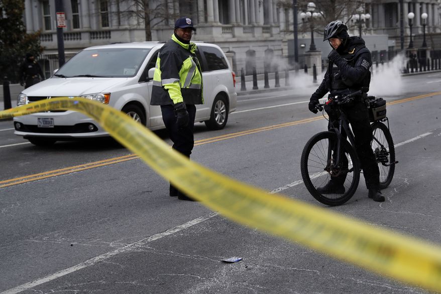 With steam from an underground grate in the background, a Metropolitan Police officer and Secret Service Police officer react to a large gust of frigid wind while blocking the road on 17th Street at the intersection with Pennsylvania Avenue near the White House in Washington, Wednesday, Jan. 30, 2019. (AP Photo/Jacquelyn Martin)