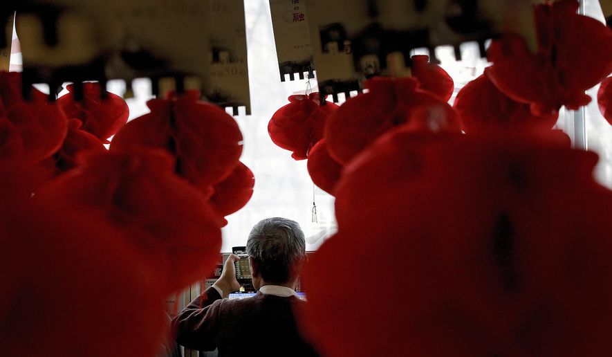 A man holds a smartphone showing stock prices as he monitors stock prices at a brokerage house decorated with red lanterns in Beijing, Friday, Feb. 1, 2019. Asian markets were mixed on Friday as trade talks ended in Washington with no deal but the promise of a second meeting between U.S. President Donald Trump and Chinese leader Xi Jinping. Gains were limited by a private survey showing that Chinese manufacturing slowed to the lowest level in almost three years. (AP Photo/Andy Wong)