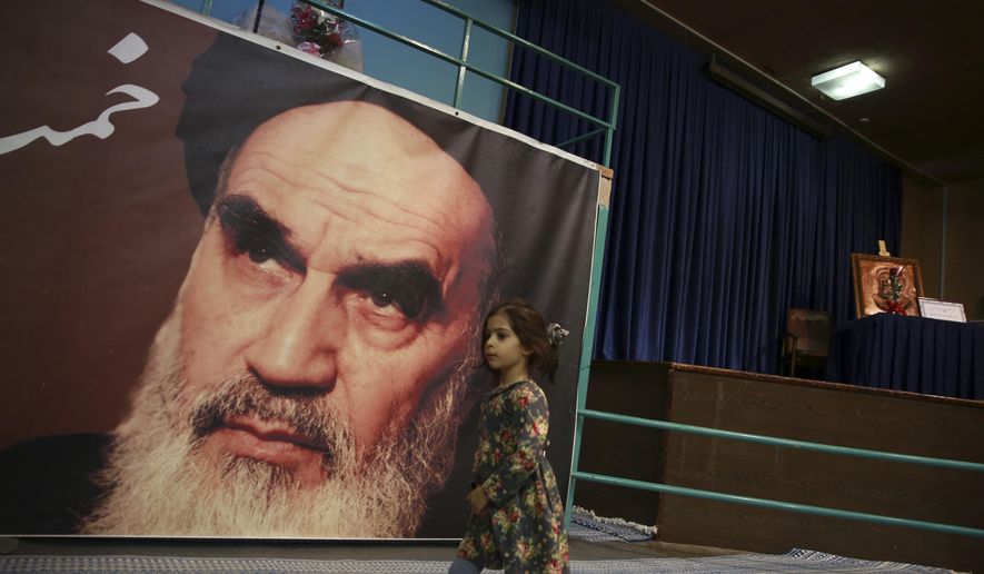 In this Tuesday, Jan. 22, 2019, photo, a girl walks past a poster of Ayatollah Ruhollah Khomeini, at a mosque where he made speeches, in northern Tehran, Iran. The memory of Khomeini, who died in 1989 at the age of 86, looms large over Tehran today. His image is on bank notes and in textbooks in Iran, often as an embodiment of the 1979 Islamic Revolution that swept aside the country’s shah and forever changed the nation. (AP Photo/Vahid Salemi)