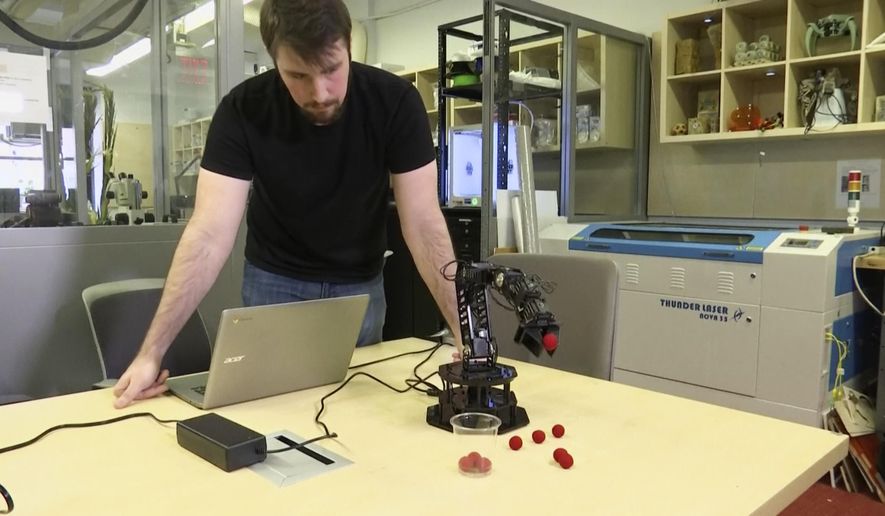 In this image made from a Feb. 1, 2019, video, Robert Kwiatkowski, a graduate student at Columbia University, demonstrates a robotic arm picking up a red ball and dropping it in a cup at the school in New York. Columbia University engineers have given a robot the ability to model itself without prior knowledge of physics or its own shape. It’s learned that it’s a robotic arm using a process of self-simulation. (AP Photo)