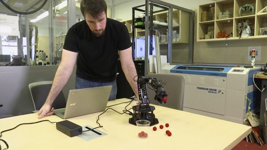 In this image made from a Feb. 1, 2019, video, Robert Kwiatkowski, a graduate student at Columbia University, demonstrates a robotic arm picking up a red ball and dropping it in a cup at the school in New York. Columbia University engineers have given a robot the ability to model itself without prior knowledge of physics or its own shape. It’s learned that it’s a robotic arm using a process of self-simulation. (AP Photo)