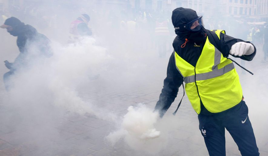 A demonstrator returns a tear gas grenade during a demonstration called by the CGT (General Working Confederation) union, Tuesday, Feb. 5, 2019 in Lille, northern France. Workers, public servants, and retired people were invited to march during a strike called by the CGT (General Working Confederation) union. (AP Photo/Michel Spingler)