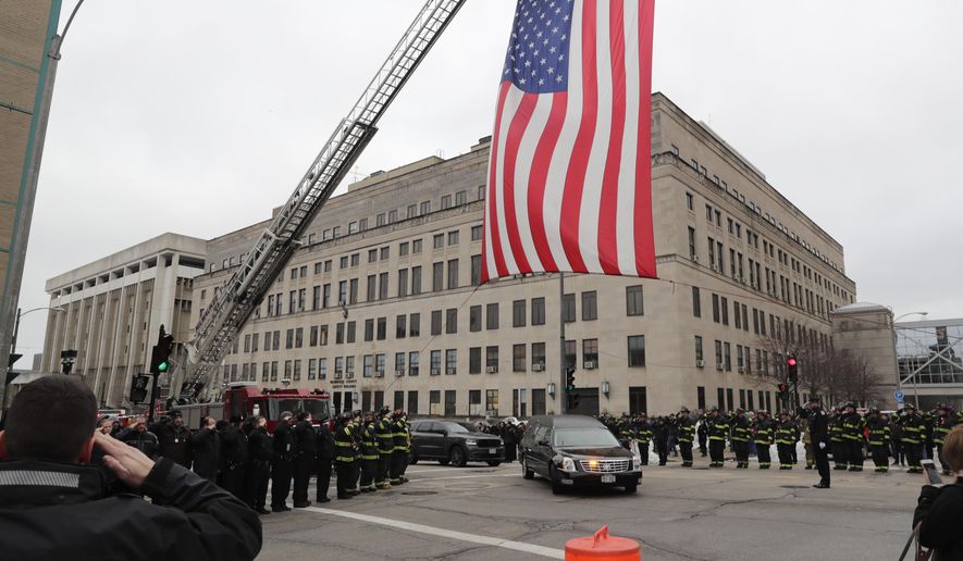 The Milwaukee Fire Department raises a flag at the intersection of 9th and State streets as the hearse containing the casket of a Milwaukee police officer drives under in Milwaukee on Wednesday, Feb. 6, 2019. The 17-year police veteran was shot and killed as he served a warrant on Milwaukee's south side Wednesday, becoming the city's third officer to be killed in the line of duty in eight months, officials said. The 35-year-old officer's name has not been released at the time of this reporting. (James B. Nelson/Milwaukee Journal-Sentinel via AP)