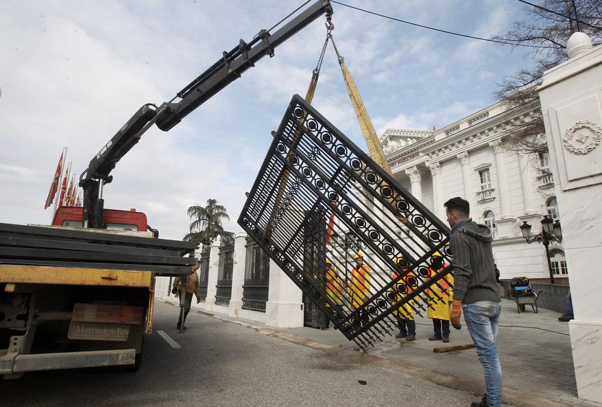 Workers use a crane to dismantle metal fencing from the front of the Macedonia's Government in the capital Skopje, Thursday, Feb. 7, 2019. Dozens of workers have started dismantling the metal fence around the Macedonian government buildings, seen as symbolic move to eradicate divisions in the country and to devalue former conservative government extravaganza. (AP Photo/Boris Grdanoski)